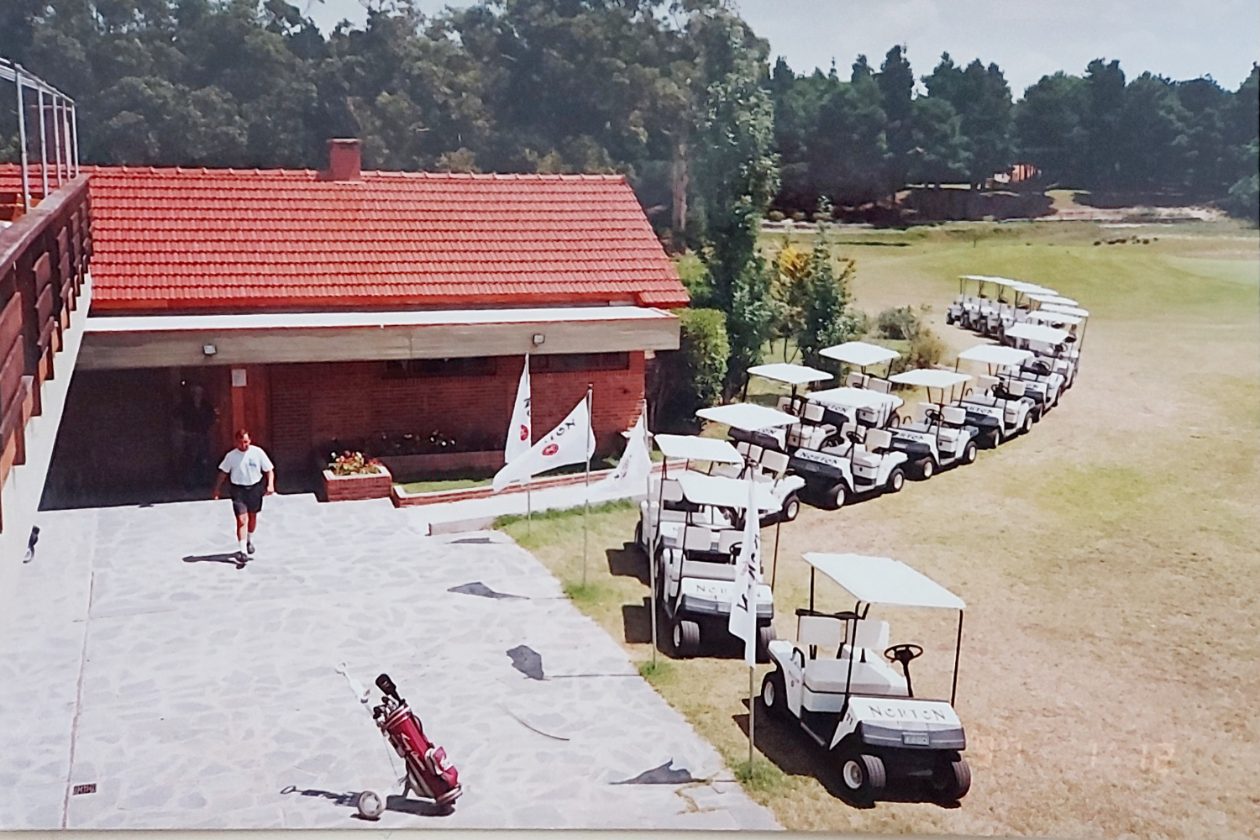 Flota de carros de golf E-Z-GO con banderas Norton frente al club house